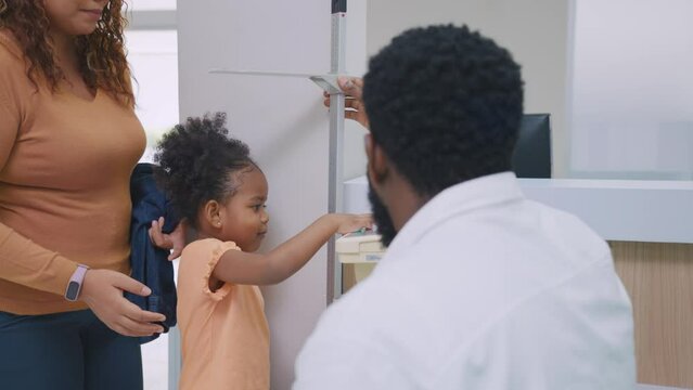 Attractive parents measuring African little girls height in hospital.