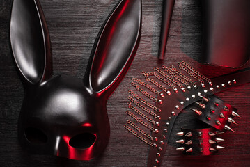 Black rabbit mask, studded leather bracelets, high heels shoes and neck choker on the black wooden table flat lay background close up. - Powered by Adobe