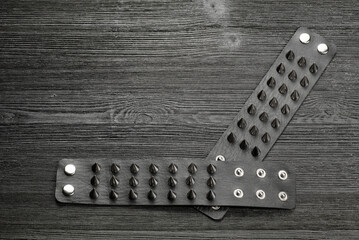 Black studded leather bracelet on the black wooden table background close up. Top view.