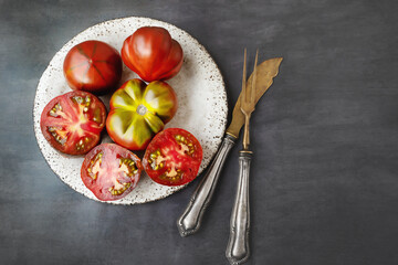 Fresh red ripe tomatoes on wooden cutting board with parsley, dark rustic background. Cut tomatoes...