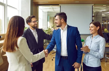Foto op Aluminium Woman shaking hands with a man celebrating success, making deal, business achievement, signing contract or greeting new employee with group of people in background standing in office. © Studio Romantic