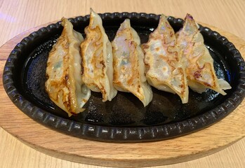 Deep-fried gyoza in black hot plate on wooden table 
