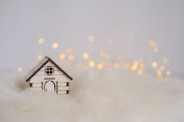 Miniature wooden house on white fur background with bokeh lights