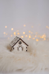 Miniature wooden house on white fur background with bokeh lights