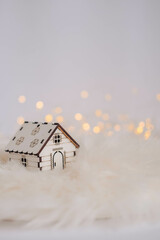 Miniature wooden house on white fur background with bokeh lights