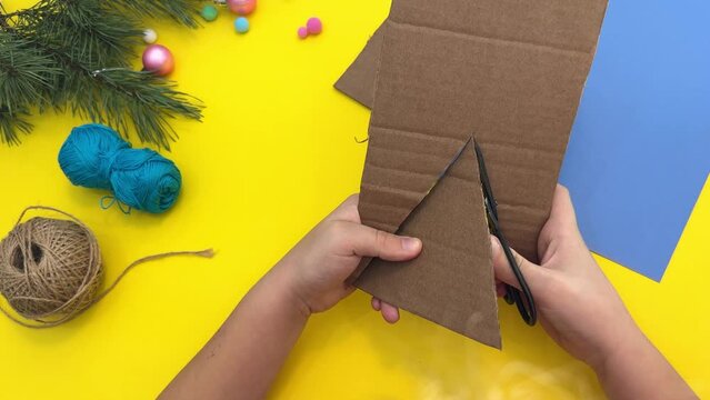 Step-by-step instructions how to made christmas tree toy a dinosaur made by a child out of cardboard and red threads. The symbol of 2024. Step 1 - cut out a triangle from cardboard.