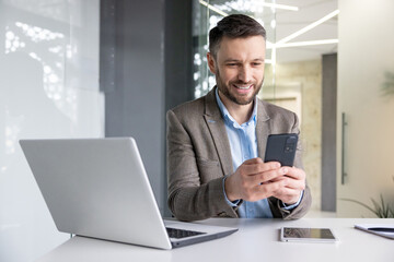 Joyful smiling satisfied businessman typing text message on phone, man in business suit browsing...
