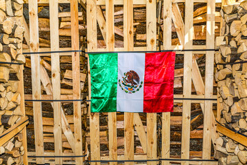 Mexican fabric flag hanging on wall of wooden containers, colors red, white, green and feathered...
