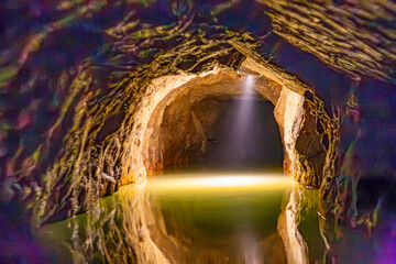 Interior of an underground river in Remouchamps caves illuminated with light of an lamp, tunnel with irregular and rough walls, reflection on water surface, hazy effect in front, Aywaille, Belgium