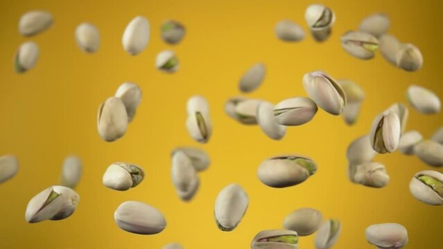 Close up of salted pistachios flying up and rotating on the yellow background