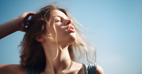 Candid portrait of young woman ruffling her messy hair against blue sky and sunlight