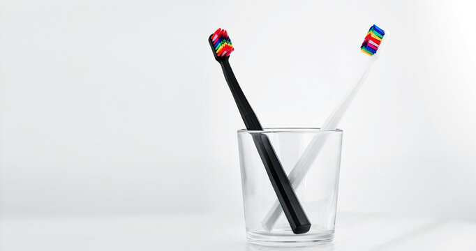 Stylish dental abacus in a glass cup. Black and White toothbrushs with multicolored bristles on white background. Bristles in all colors of the rainbow. Rainbow toothbrush Fashionable oral care