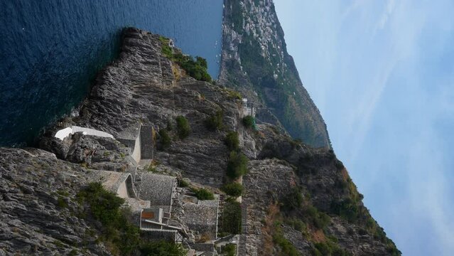 Vertical stunning view over Amalfi coast in Italy with picturesque Praiano village, steep stone staircase on steep cliff, on sunny summer day with beautiful seascape and blue sky, slow motion.