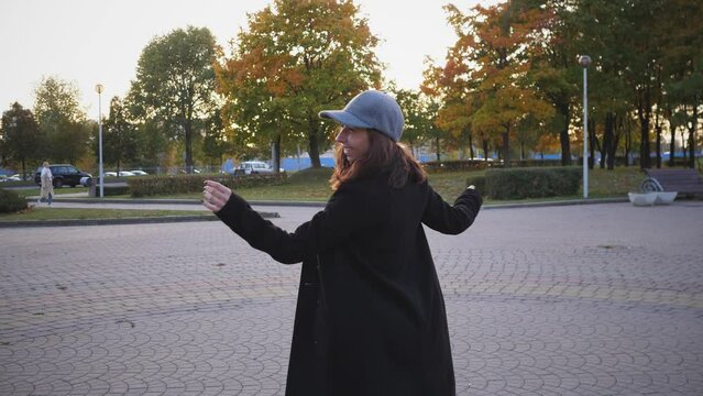A happy stylish girl in a coat in the spring spins in a city park and rejoices