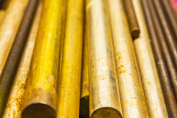 Large bronze round bars and steel threaded rods lie on a shelf, close-up.
