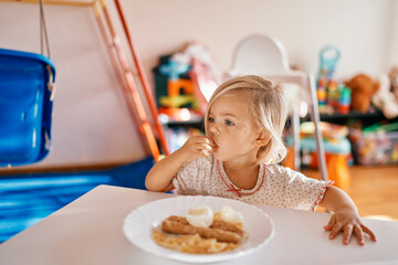Little girl sits at the table and eats breakfast with her hands
