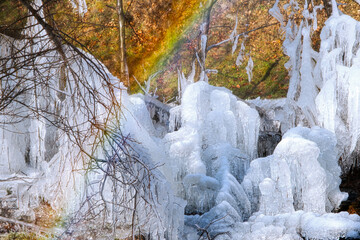 the water from the broken pipe forms ice shapes and rainbow on the edge of the river and autumn forest - Powered by Adobe