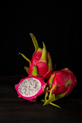 View of three pink pitayas or dragon fruits, one open, on table and black background, vertical,...