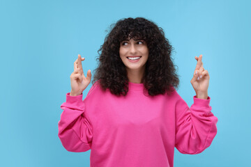 Woman crossing her fingers on light blue background