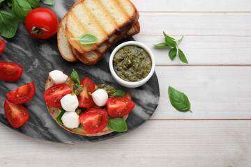 Delicious Caprese sandwich with mozzarella, tomatoes, basil and pesto sauce on white wooden table, top view