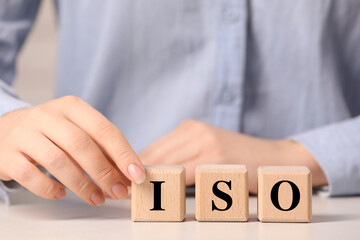 Woman making abbreviation ISO of wooden cubes at white table, closeup