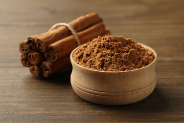 Aromatic cinnamon powder and sticks on wooden table, closeup