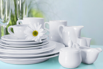Set of clean dishware and flower on light blue table, closeup
