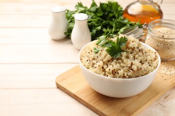Tasty quinoa porridge with parsley in bowl on light table. Space for text