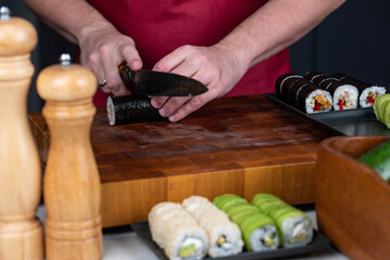 Sushi chef hands making Japanese food. Man cooking sushi at restaurant or at home. Traditional asian rolls on cutting board. Maki sushi with tuna, omelette, cheese and vegetables