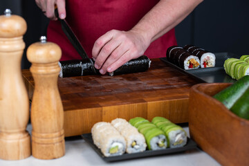 Obraz premium Sushi chef hands making Japanese food. Man cooking sushi at restaurant or at home. Traditional asian rolls on cutting board. Maki sushi with tuna, omelette, cheese and vegetables