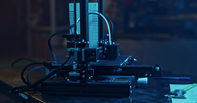3D printer with filament spool making plastic detail in dark garage