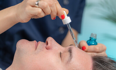 Skilled cosmetician gently applies a hyaluronic acid serum to a middle-aged man's face, promoting...