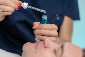 A skilled cosmetician expertly applies a hyaluronic acid serum to a middle-aged man's face, a...