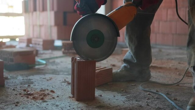 Detailed slow motion footage of sawing red bricks with a circular saw, highlighting the saw, bricks, and the worker's feet, close-up.