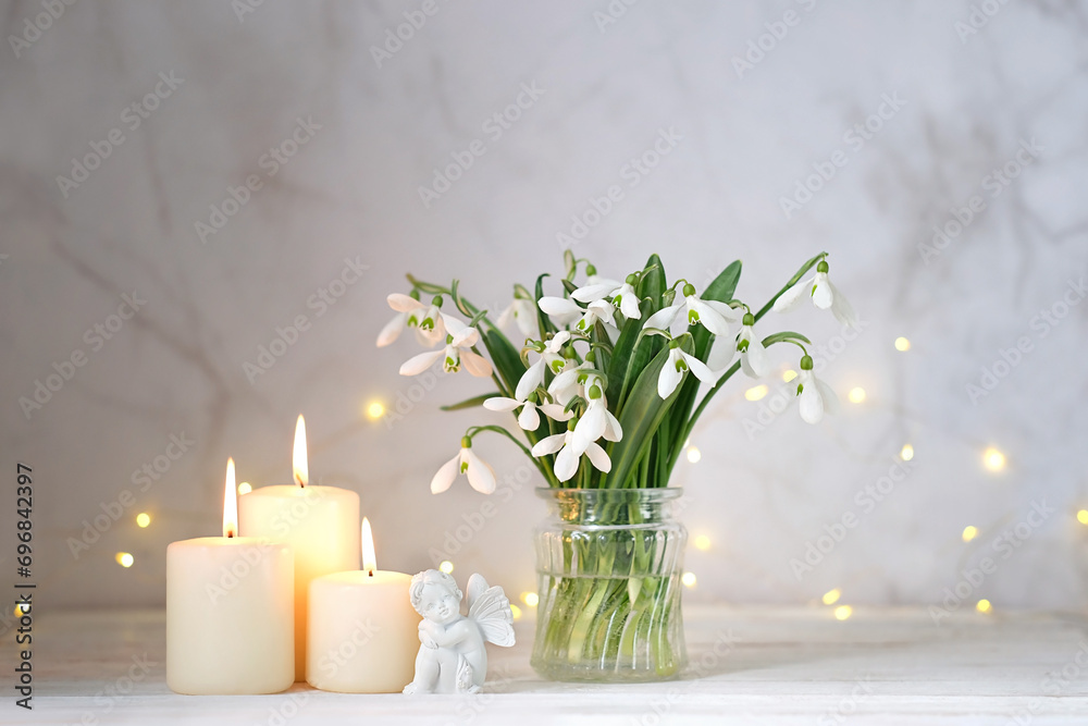 Wall mural fairy girl figurine, snowdrops flowers and candles on table, light abstract background. spring seaso