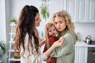 Fototapeta premium beautiful caring lesbian couple holding their baby girl in hands and comforting her, family concept