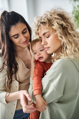 loving lgbt couple holding their adorable baby girl in hands and comforting her, family concept