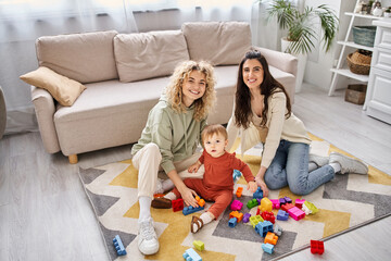 happy loving lesbian couple playing with toys with their toddler daughter at home, modern parenting