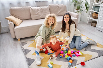 jolly loving lesbian couple playing with toys with their toddler daughter at home, modern parenting