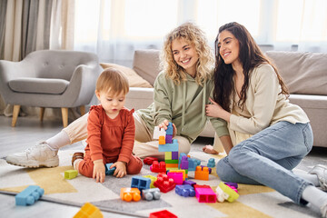 happy beautiful lesbian couple playing with their toddler daughter at home, modern parenting