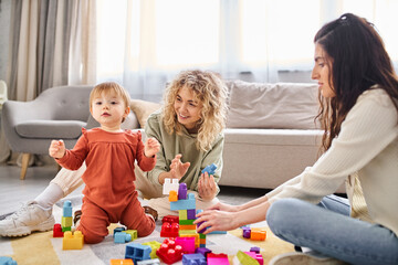 Naklejka premium joyful lesbian couple playing with their baby girl with toys on floor at home, family concept