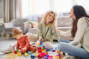 cheerful caring lgbt couple playing with their baby girl with toys on floor at home, family concept
