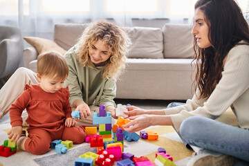 happy lesbian couple playing with their baby girl with toys on floor at home, family concept