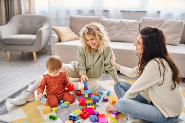 cheerful attractive lesbian couple playing with their toddler daughter at home, modern parenting