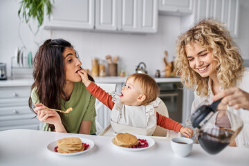 joyous beautiful lgbt couple having delicious breakfast with their baby girl, family concept