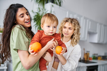Fototapeta na wymiar jolly pretty lgbt couple having fun together with their cute baby girl holding tangerines, family