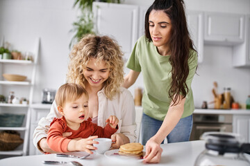 jolly beautiful lgbt couple in homewear having great time with their daughter at breakfast, family