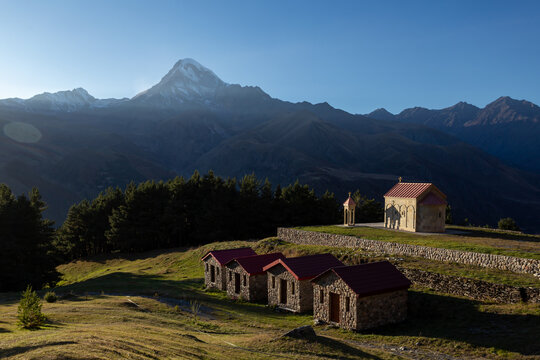 Sunset in the mountains, the territory of the monastery and the church against the background of the snow-capped peak of Kazbek stratovolcano