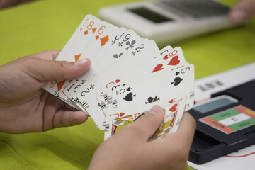 Hands of unrecognizable people play a game of bridge cards on a green table