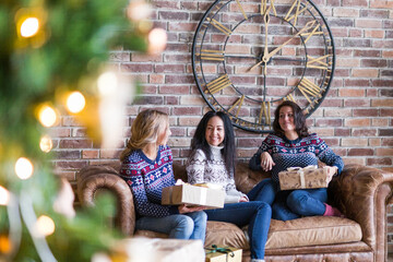 Young women surprising each other with Christmas gift while sitting on sofa in loft